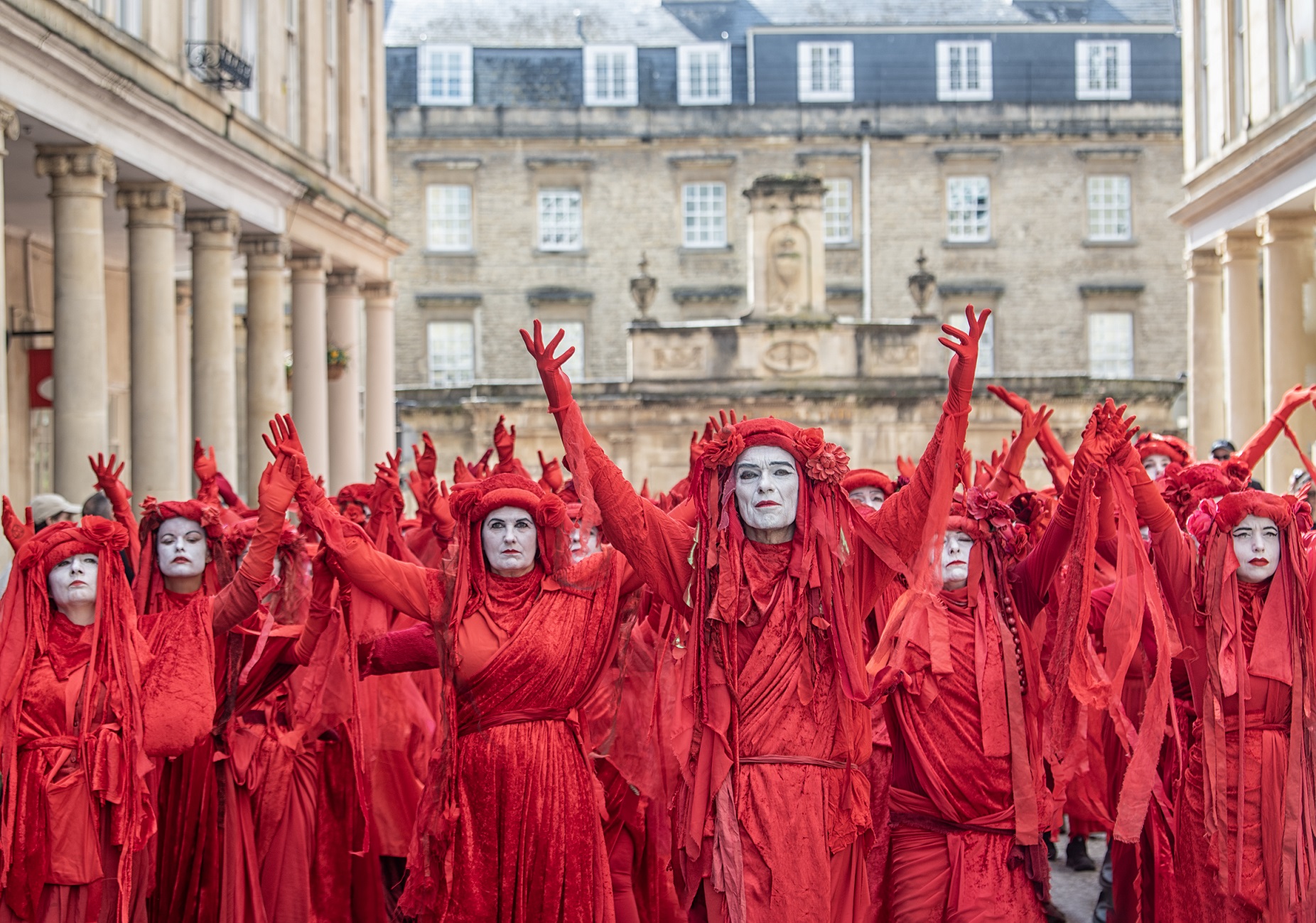 A crowd of people dressed in red robes with faces painted white taking part in 'A Funeral for Nature' theatrical event